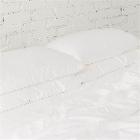 Three white pillows stacked on a bed with a white textured blanket, against a brick wall background.