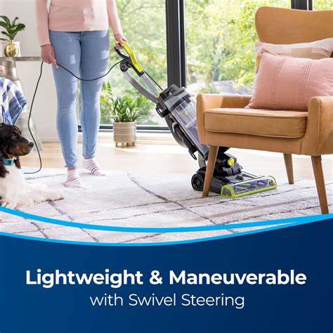 Top 2025 Stick and Upright Vacuums: Expert Picks 3 A person vacuuming a carpet with a corded upright vacuum cleaner featuring swivel steering, beside a dog and a cozy living room setting.